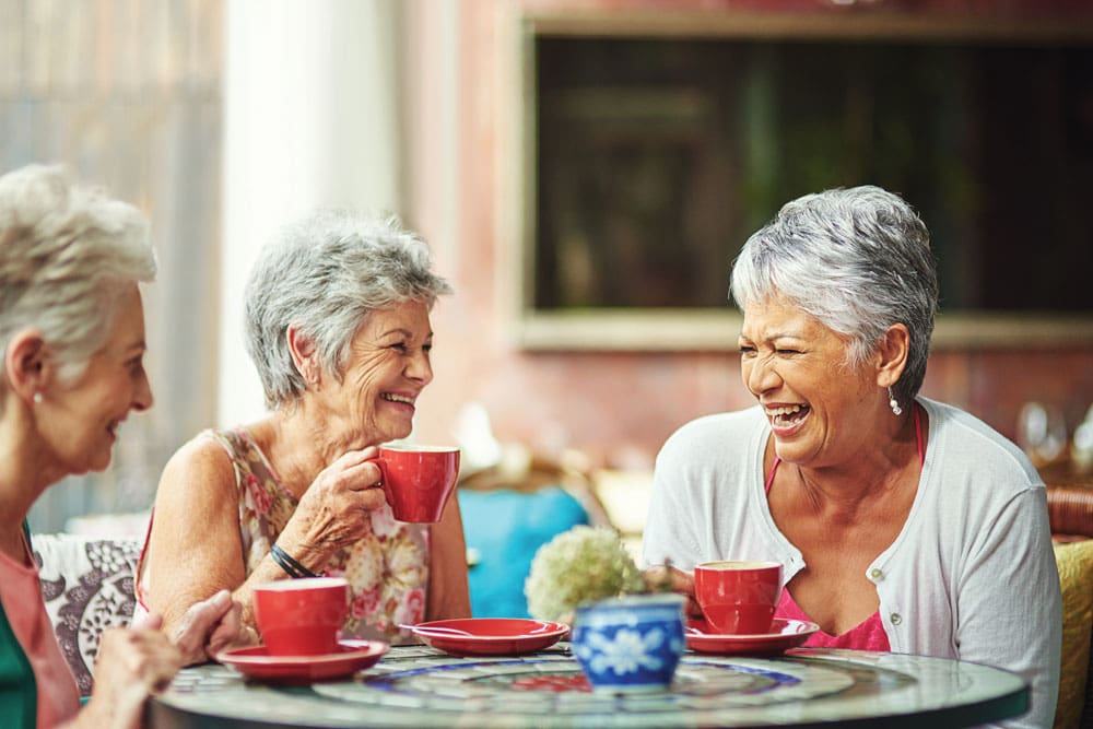 Community Lifestyles: memory care residents laughing together over cups of tea